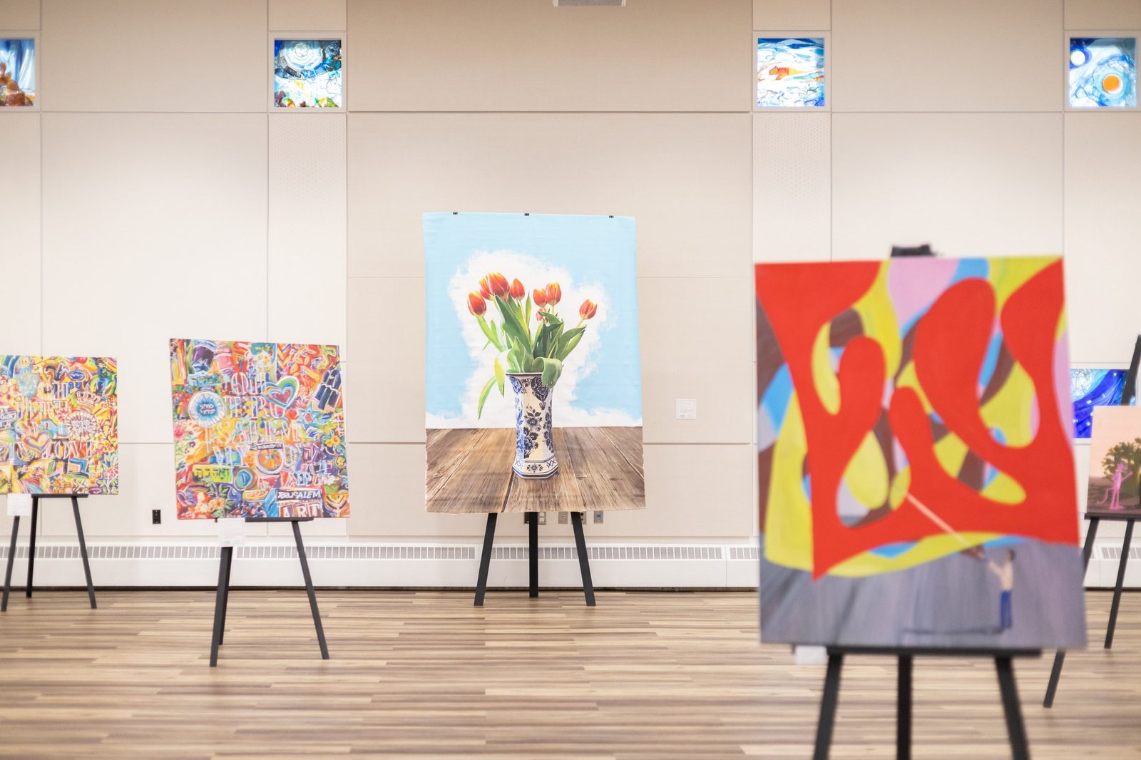 The Colours of Hope exhibition hall, with works on easels around a large tulip still life